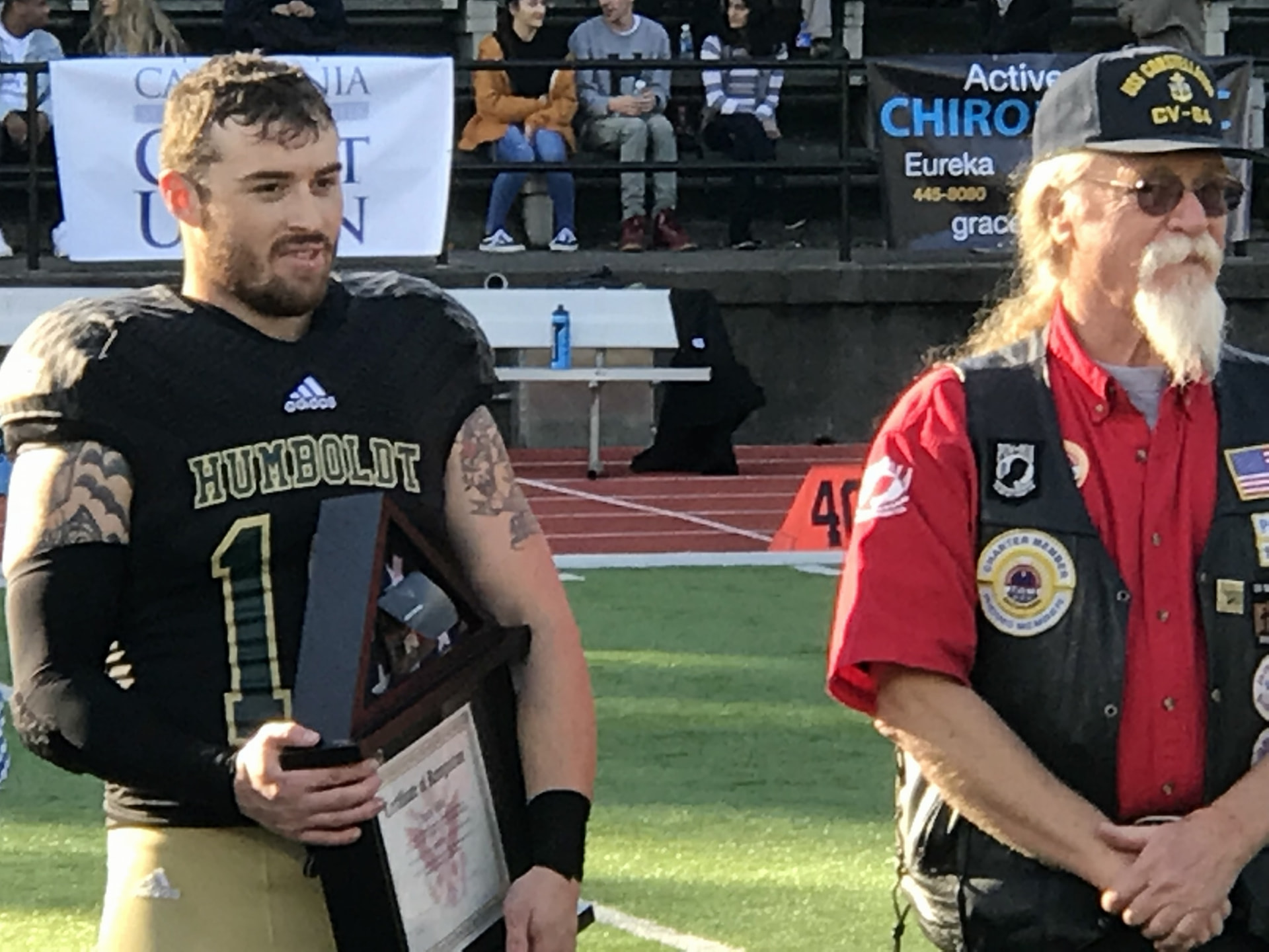 A Humboldt Heroes honoree holding a framed flag case on the football field